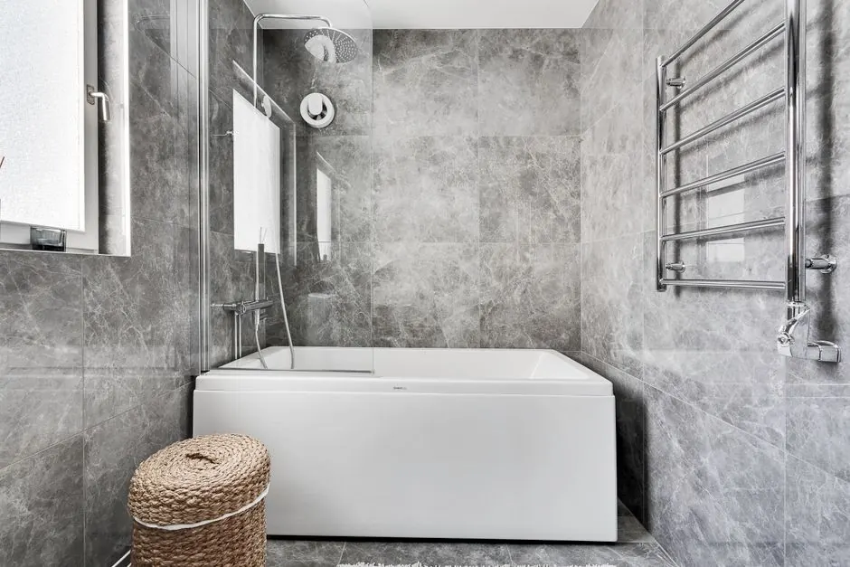 Grey tiled bathroom with a bath, glass shower screen and chrome towel rail