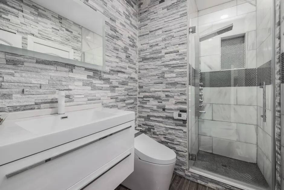 Compact bathroom with stone-effect wall tiles, a wall-hung basin and glass shower